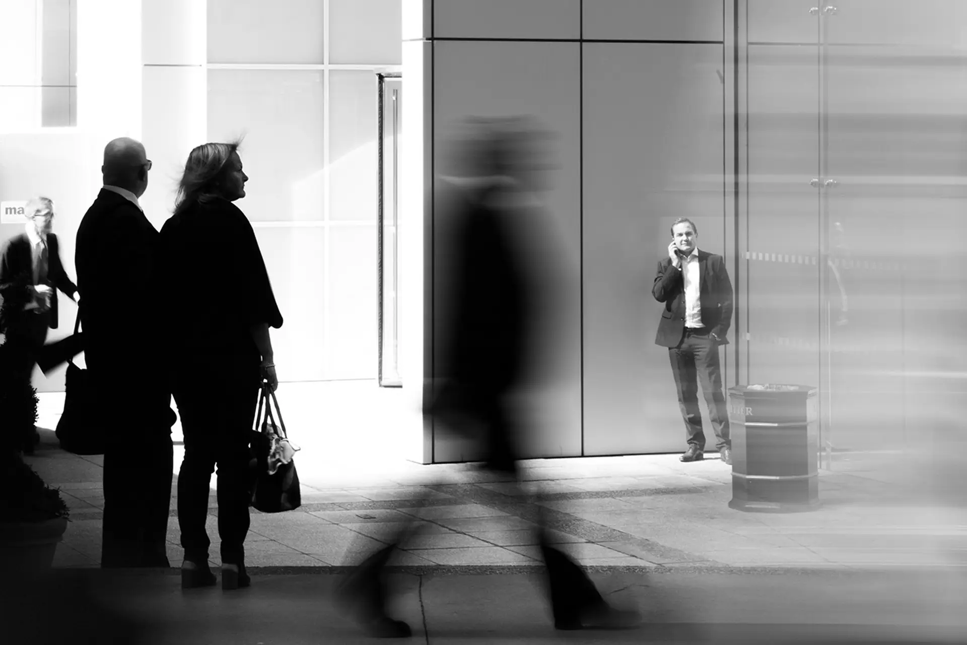 Black-and-white street scene of business professionals outside a modern office building, one taking a phone call