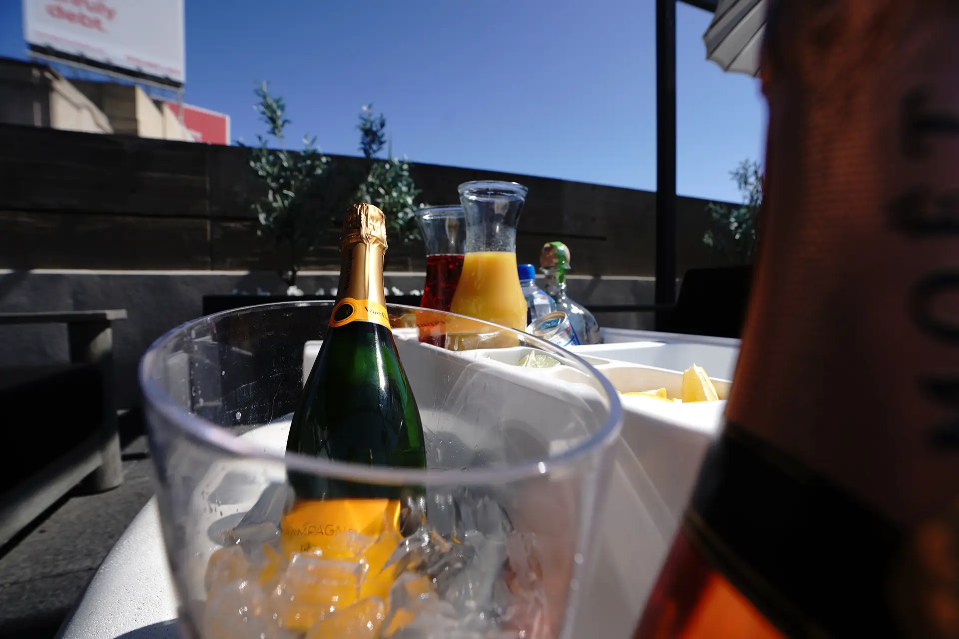 Champagne bottle chilling in an ice bucket beside carafes of orange and red juice on a sunny rooftop terrace