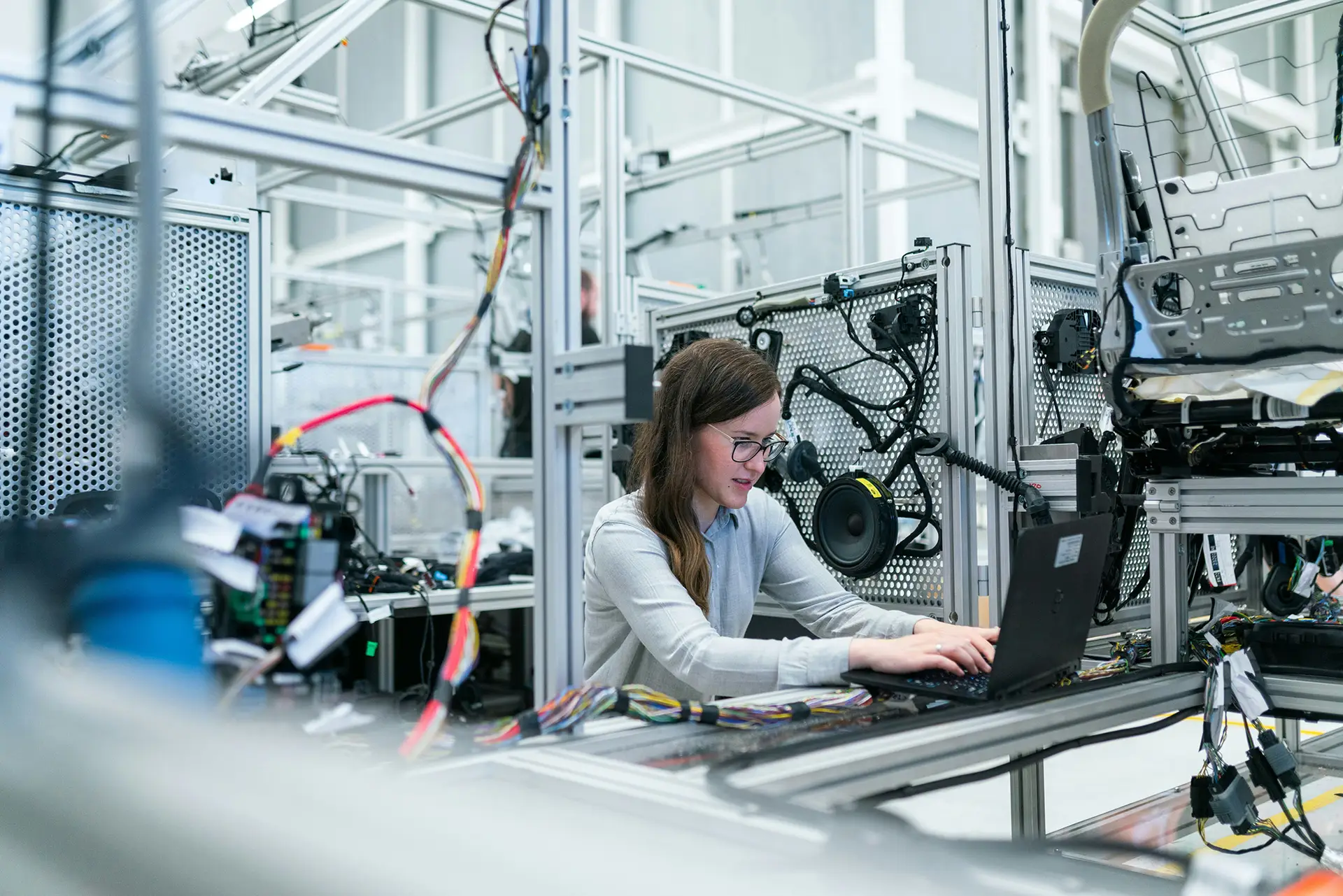 Engineer working on a laptop at an aluminum test rig surrounded by wiring harnesses and components