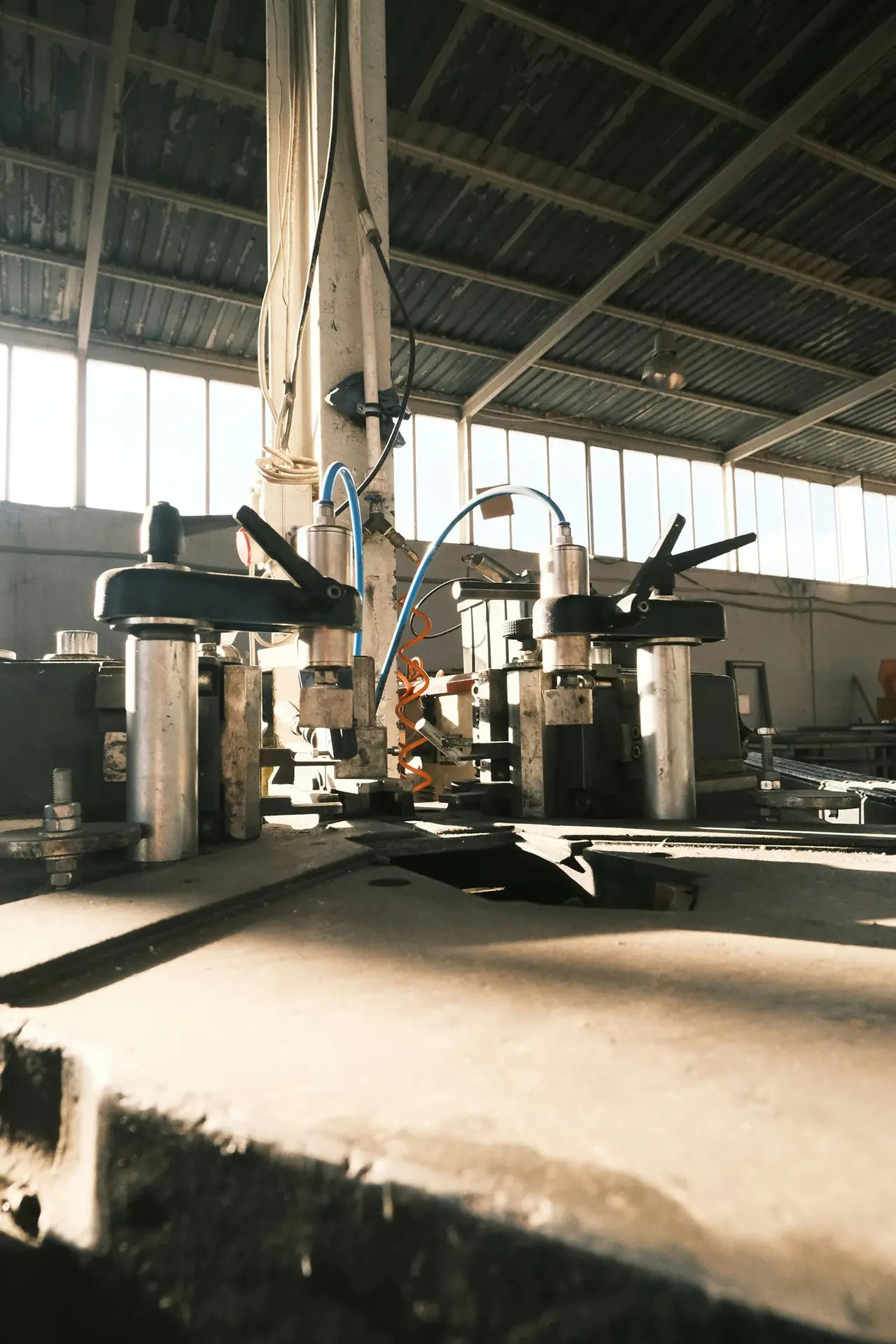 Pneumatic clamping fixtures on a steel machine table inside a sunlit factory hall