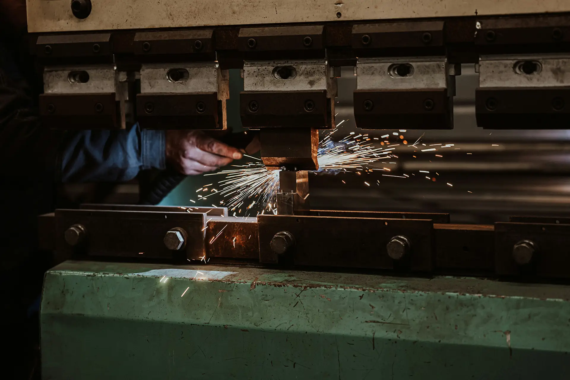 Sparks fly as a gloved hand guides metal through a press brake