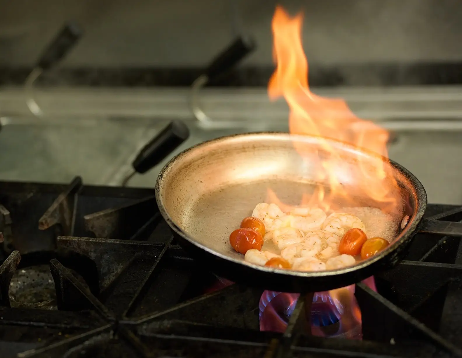 Chef flambéing shrimp and tomatoes in a pan over a commercial stove